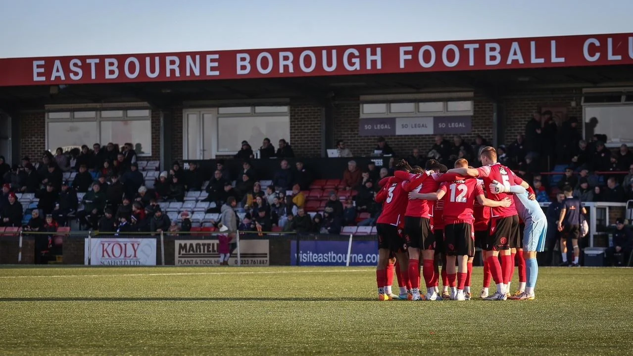 Eastbourne Borough FC players gathered in a team huddle beneath the club stand
